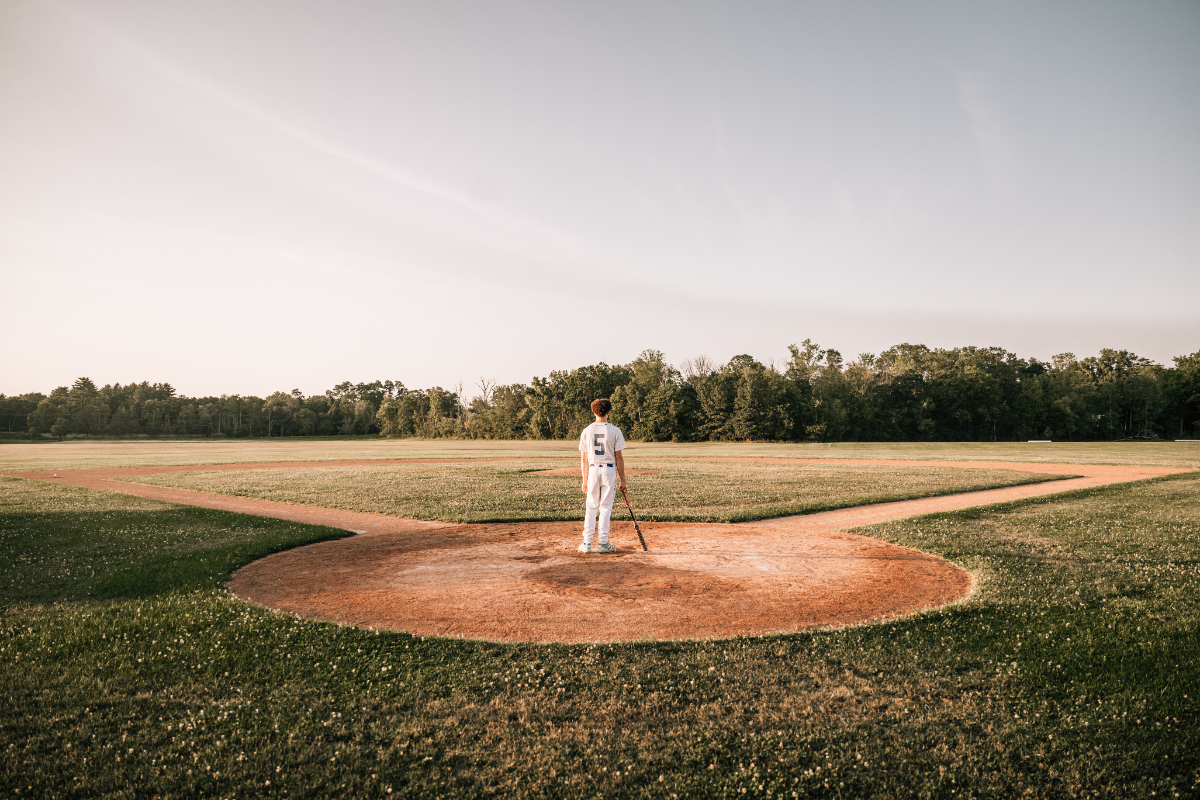 Senior pictures of baseball player standing on pitcher’s mound in wide open field at sunset