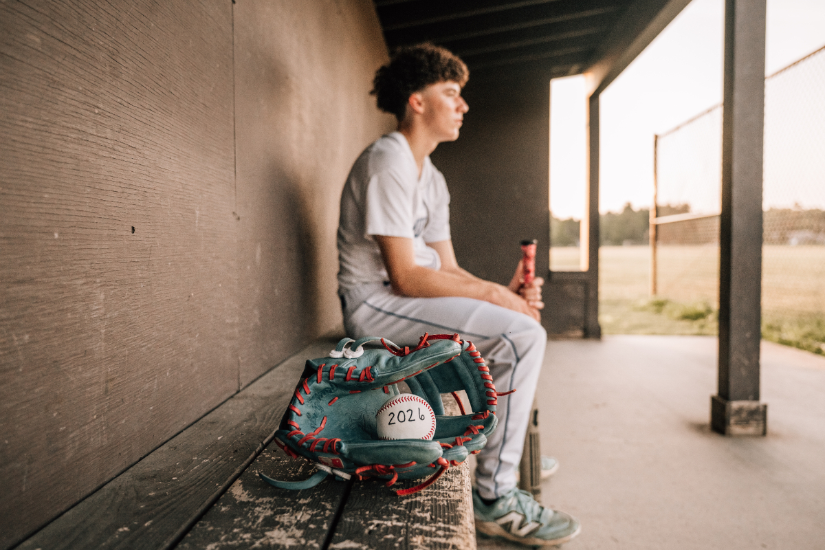 Senior pictures of baseball player sitting in dugout, glove and ball marked 2026 in foreground