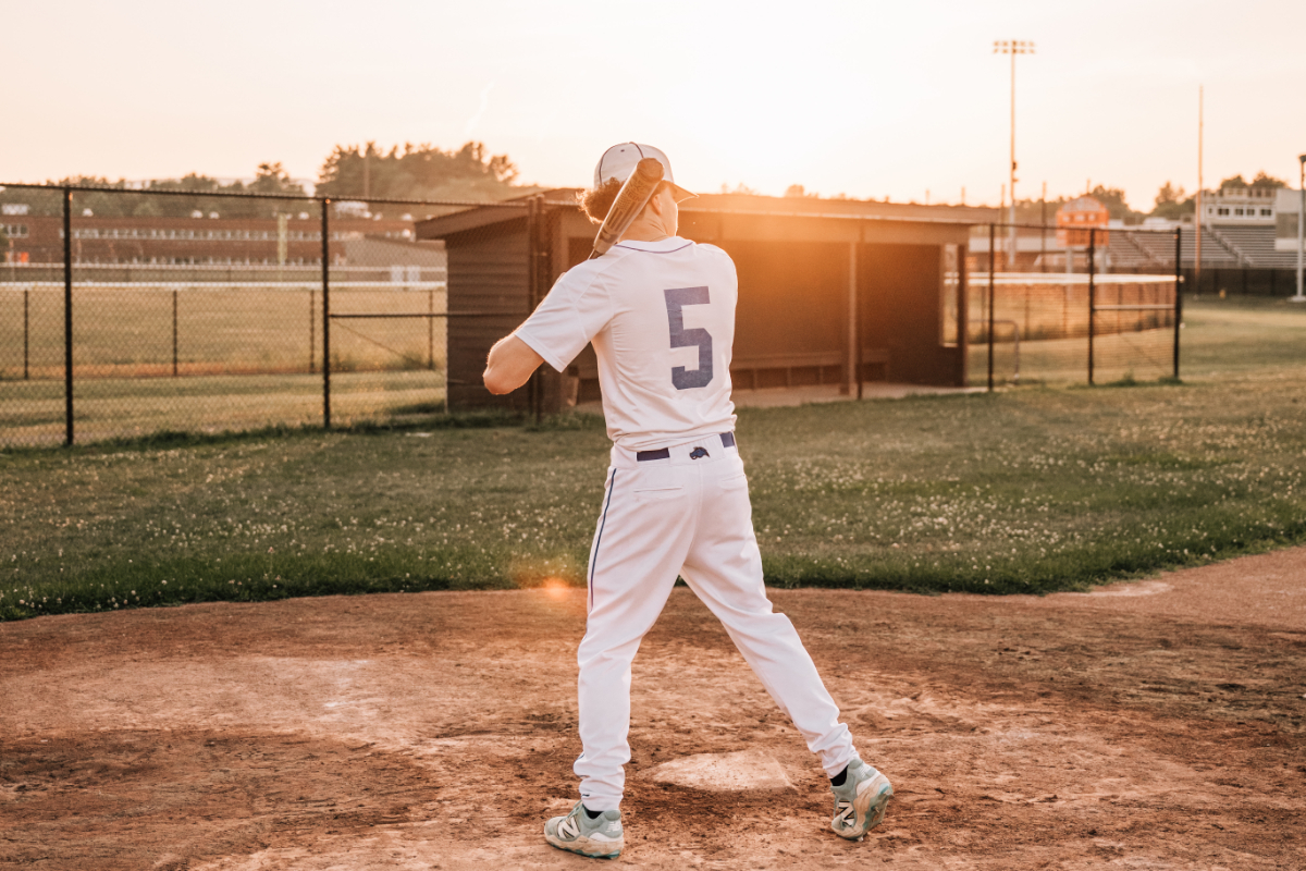 Senior pictures of baseball player swinging bat during golden hour on high school field