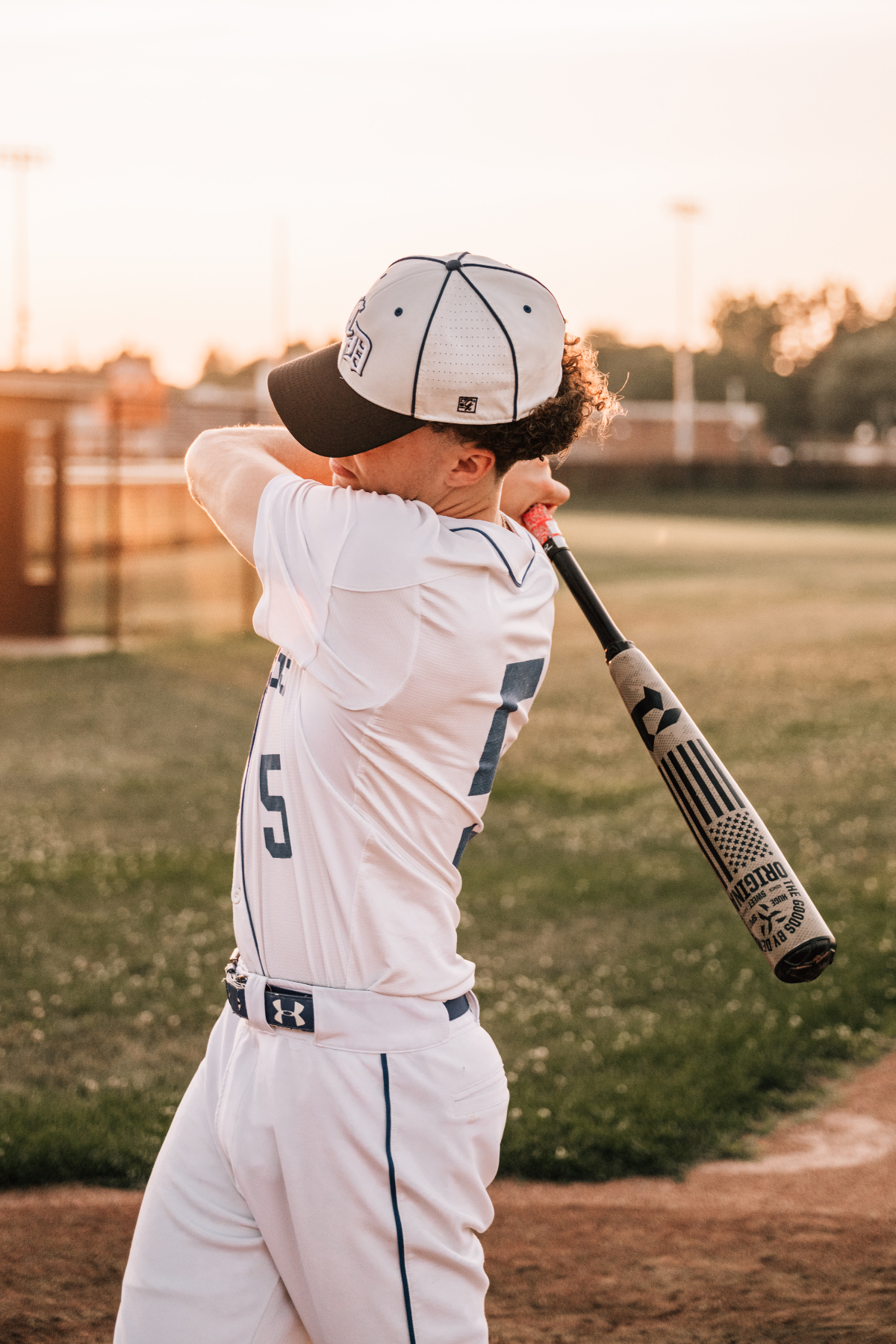 Senior pictures of a baseball player swinging bat during golden hour outdoor sports session