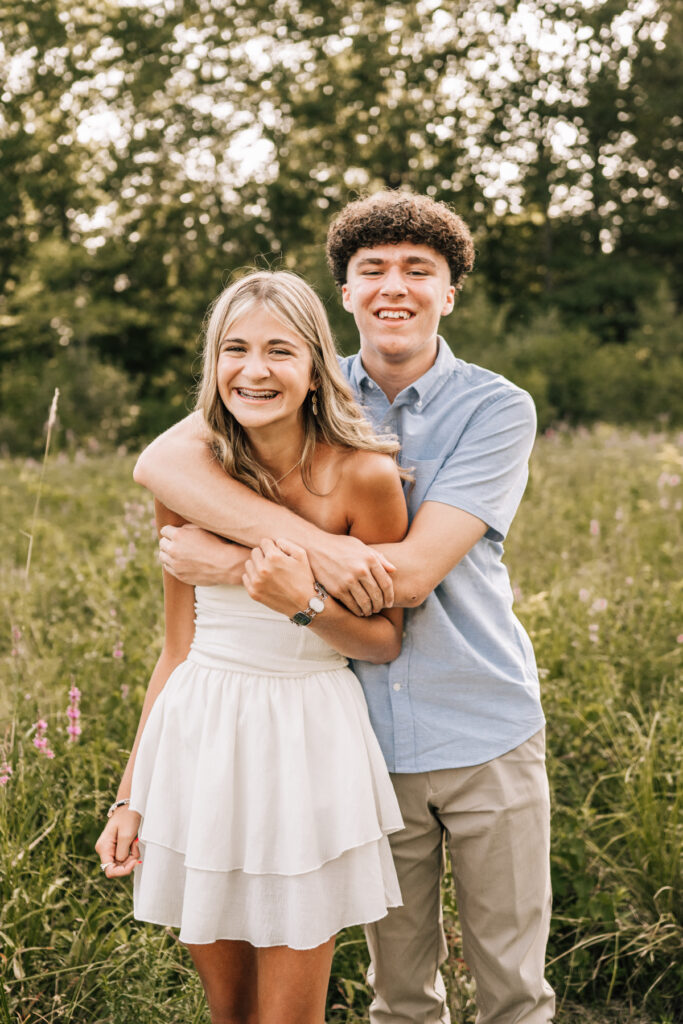 Teen siblings and parent hugging and laughing outdoors in tall grass, candid connection and playful moments