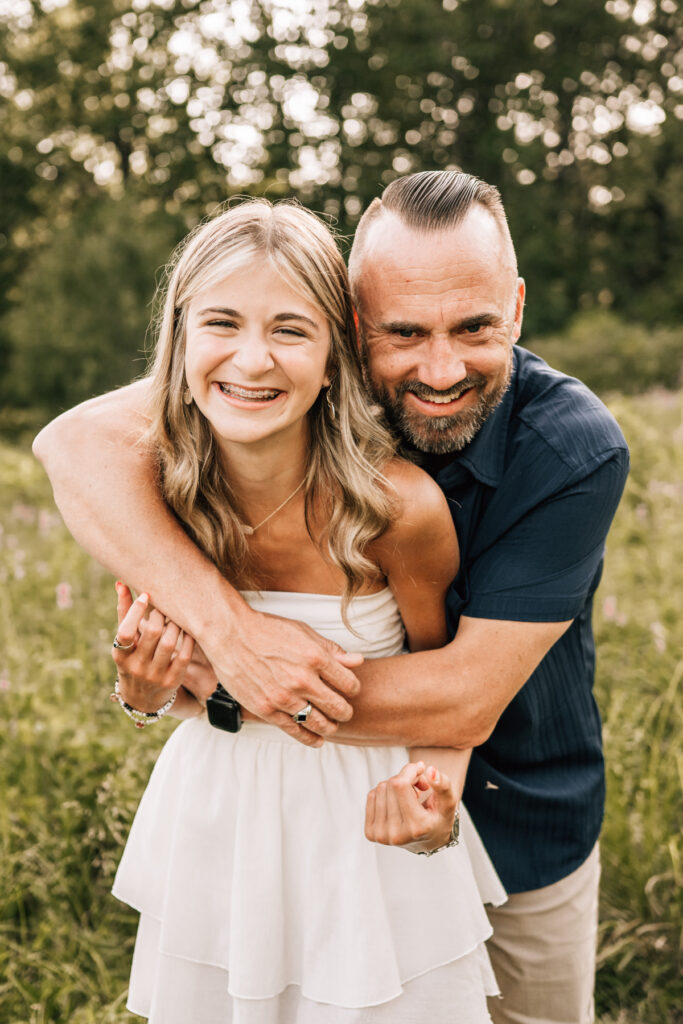 Father hugging daughter, both smiling close together in natural light, relaxed and joyful moment