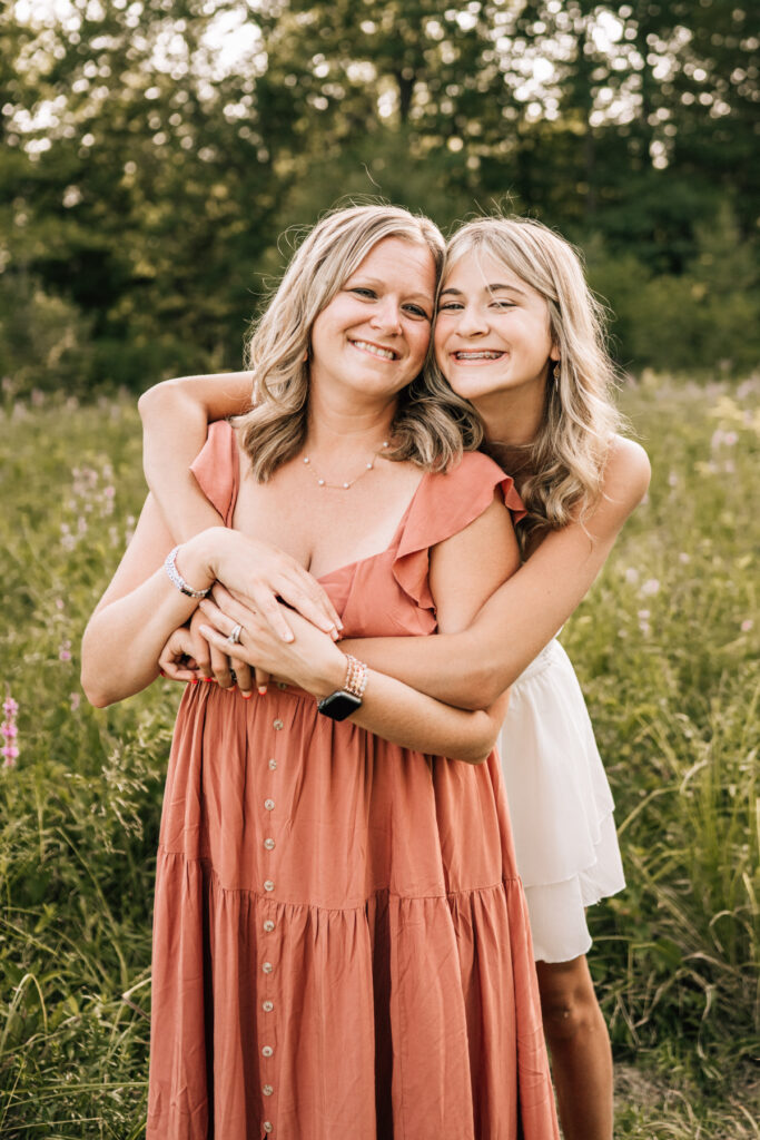 Mother and daughter embracing and smiling, warm outdoor setting with soft light and genuine connection