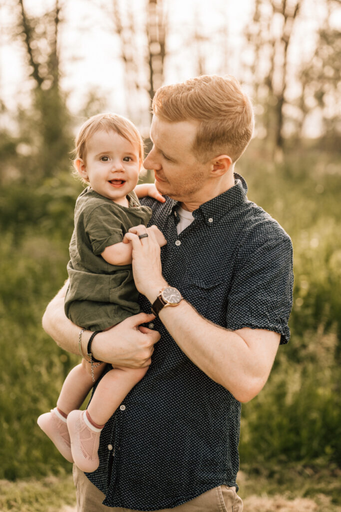 Spring family photos of happy baby in denim overalls smiling in soft natural light outdoors