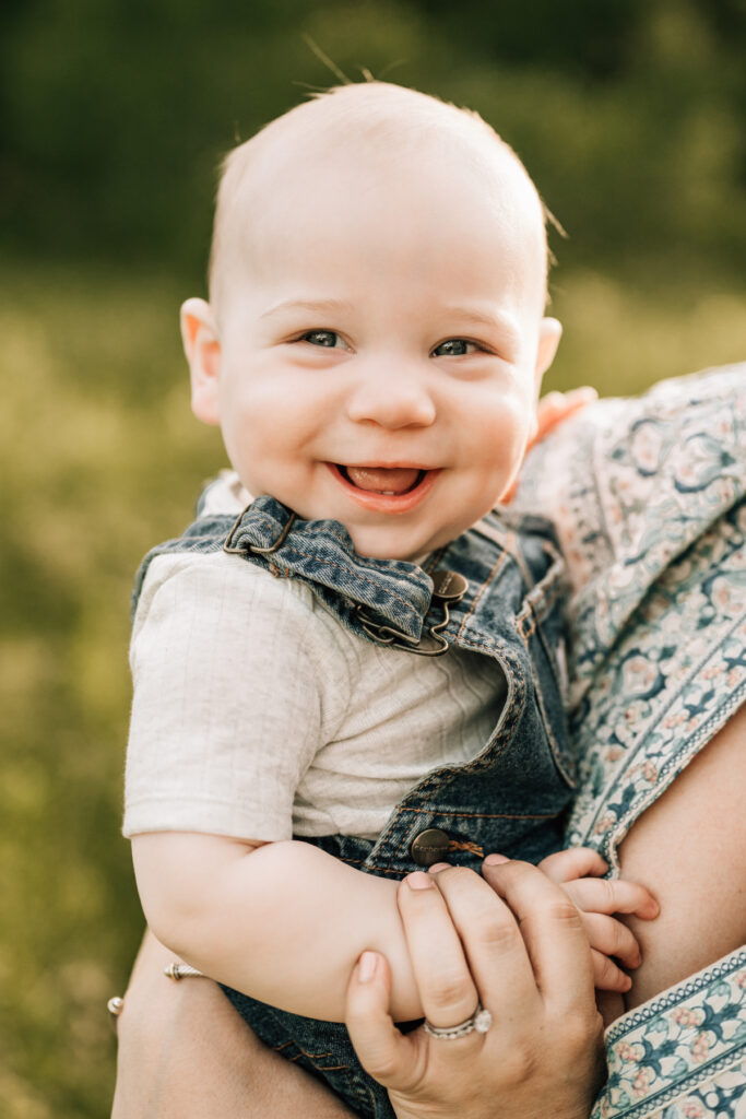 Spring family photos of happy baby in denim overalls smiling in soft natural light outdoors