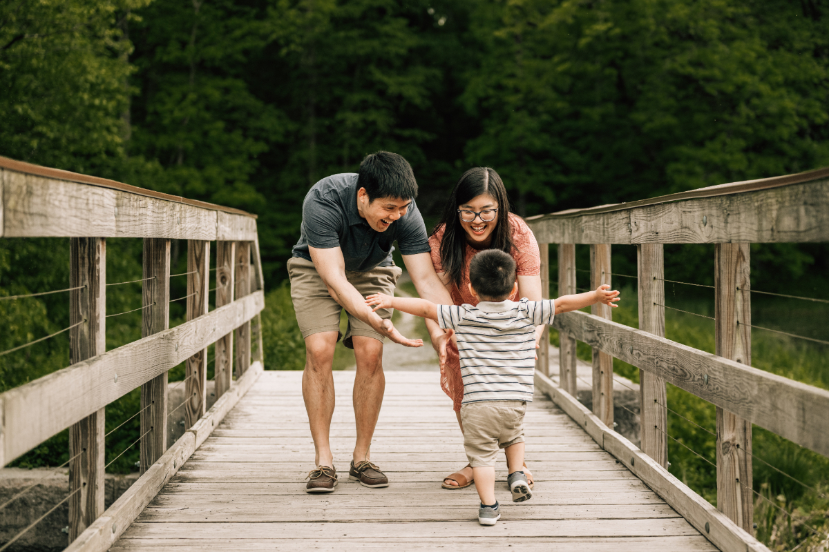 Parents holding child’s hands while walking on wooden bridge, playful and candid family moment outdoors