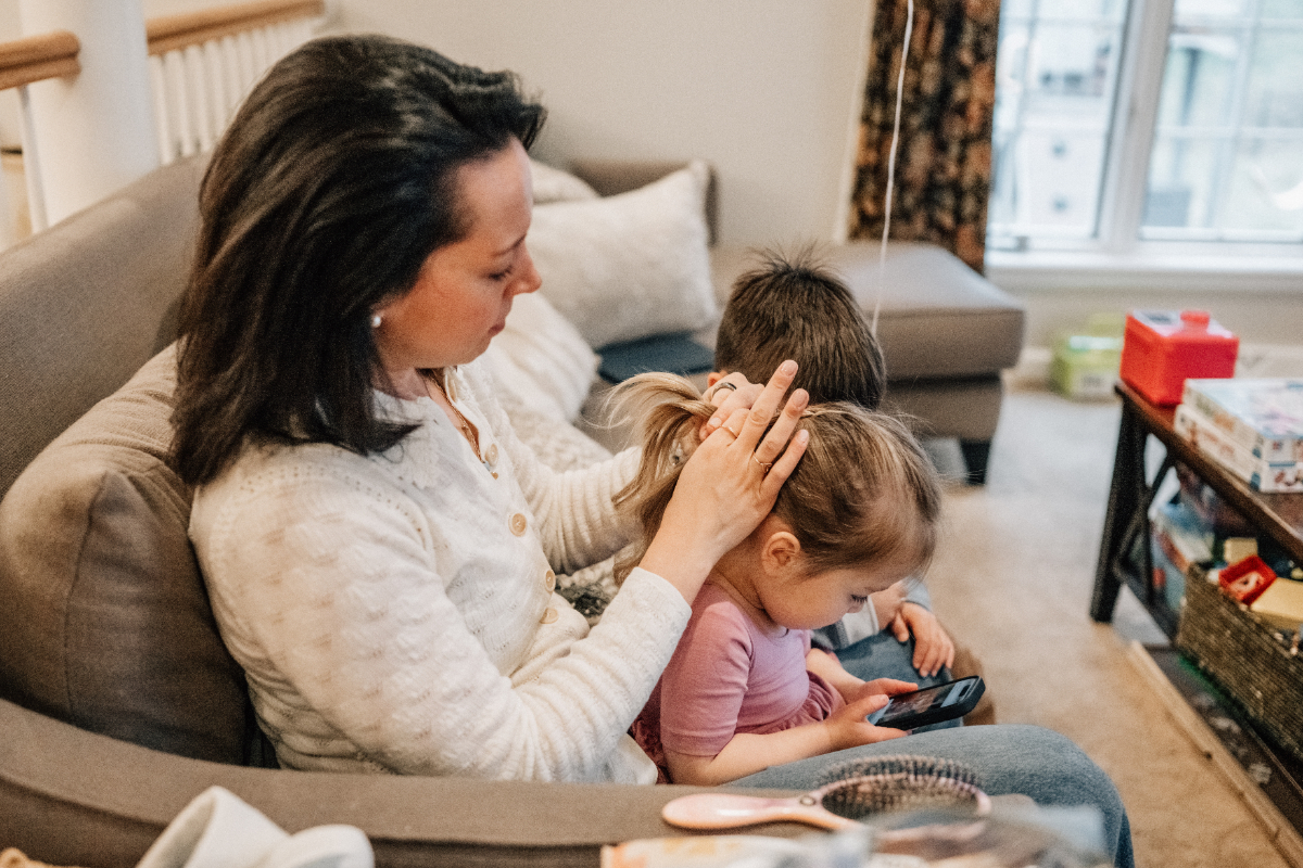 Family of four laughing together in grassy field, parents lifting child in joyful, connected moment