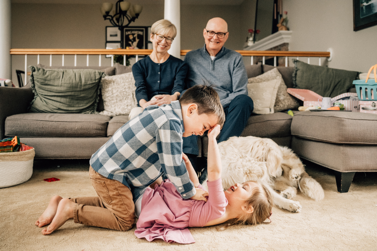 Children wrestling and laughing on floor while grandparents watch, playful and connected family scene