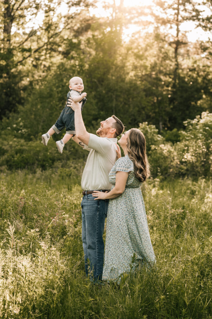 Father lifting toddler into the air while mother smiles nearby, warm and playful outdoor family moment