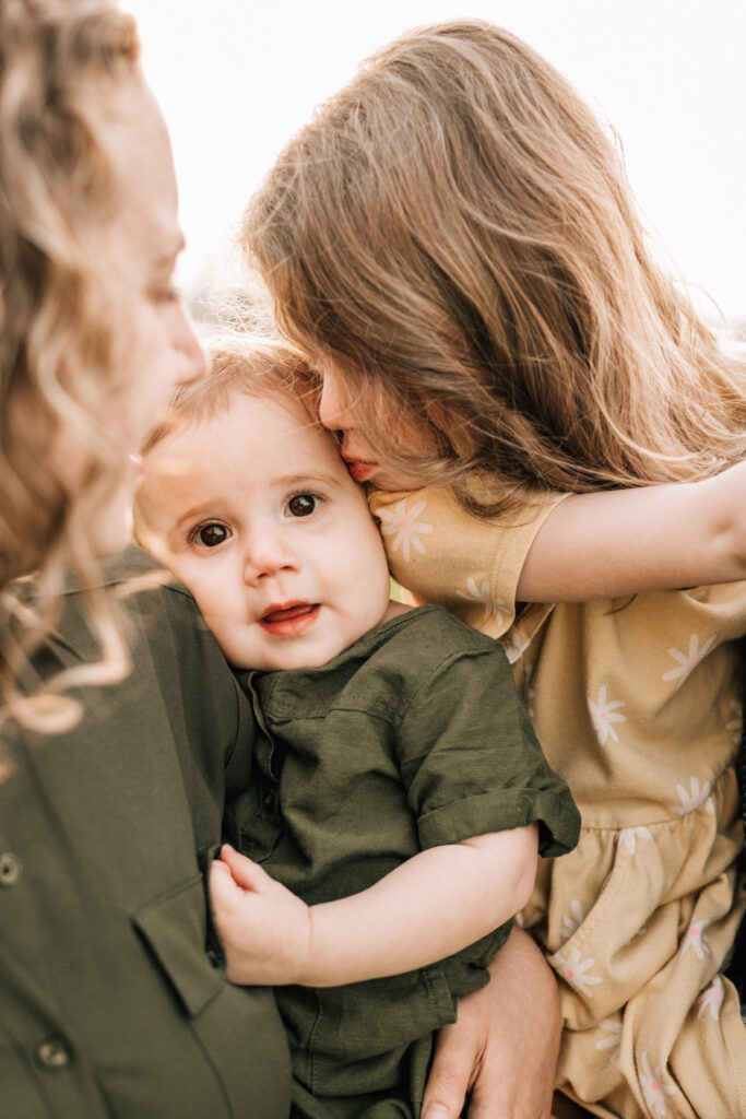 Spring family photos of mom holding smiling baby in warm sunlight, sharing candid, joyful moment outdoors