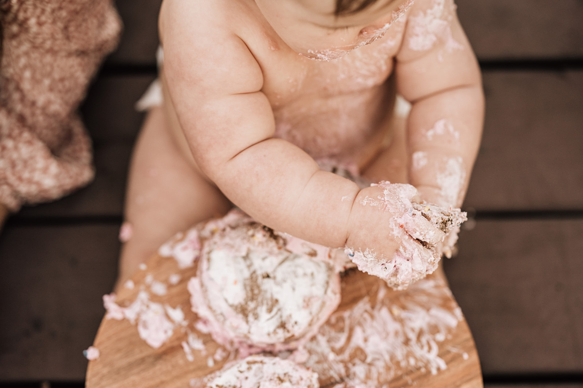 Close-up of baby’s hands covered in cake and frosting, capturing messy playful moment