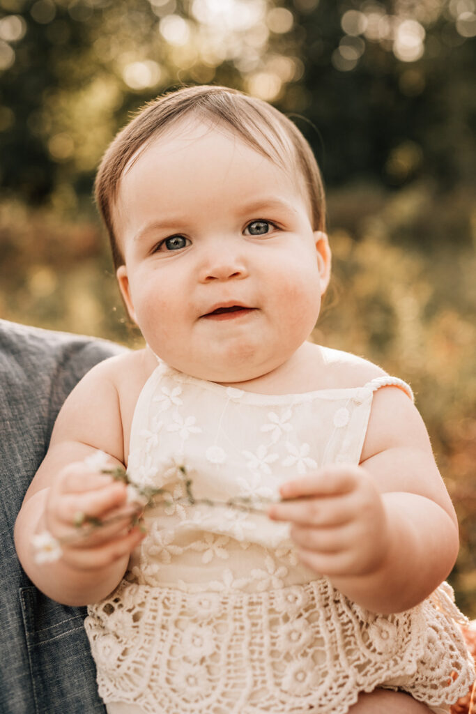 Close-up of baby holding flowers during baby’s first birthday session in soft natural light