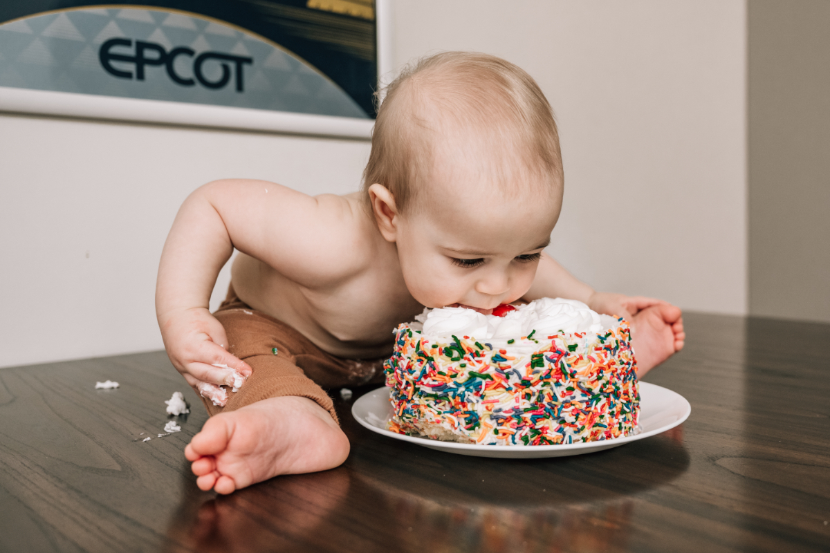 Baby leaning into cake during baby’s first birthday with colorful sprinkles and messy hands