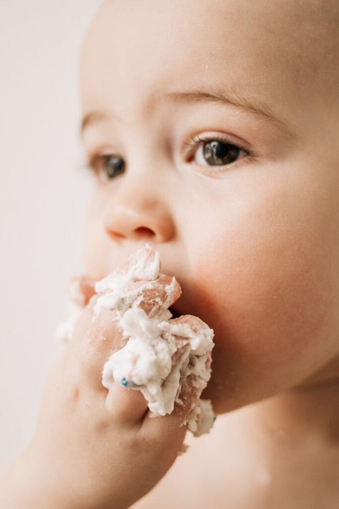 Close-up of baby eating frosting during baby’s first birthday with soft light and detail