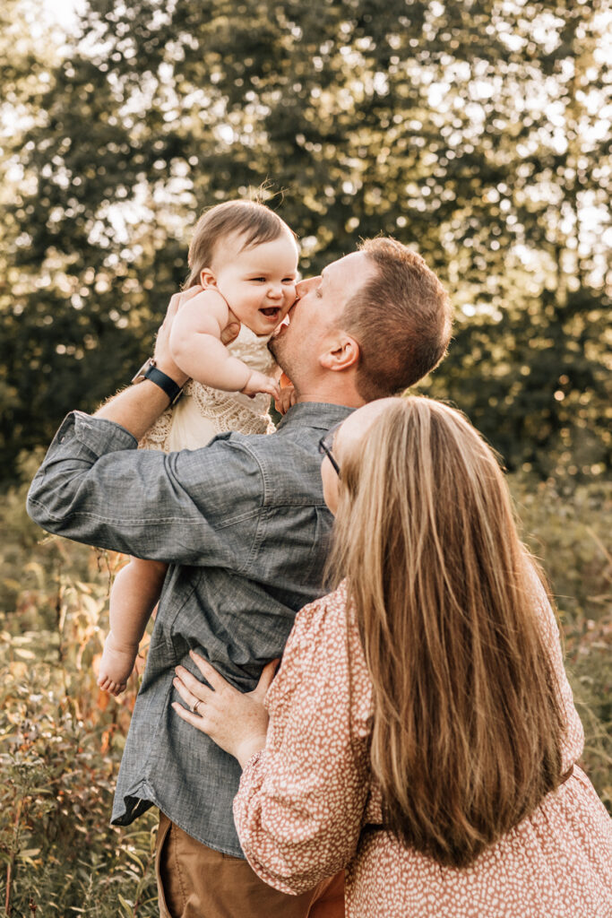 Parents lifting baby in air during baby’s first birthday session filled with laughter outdoors