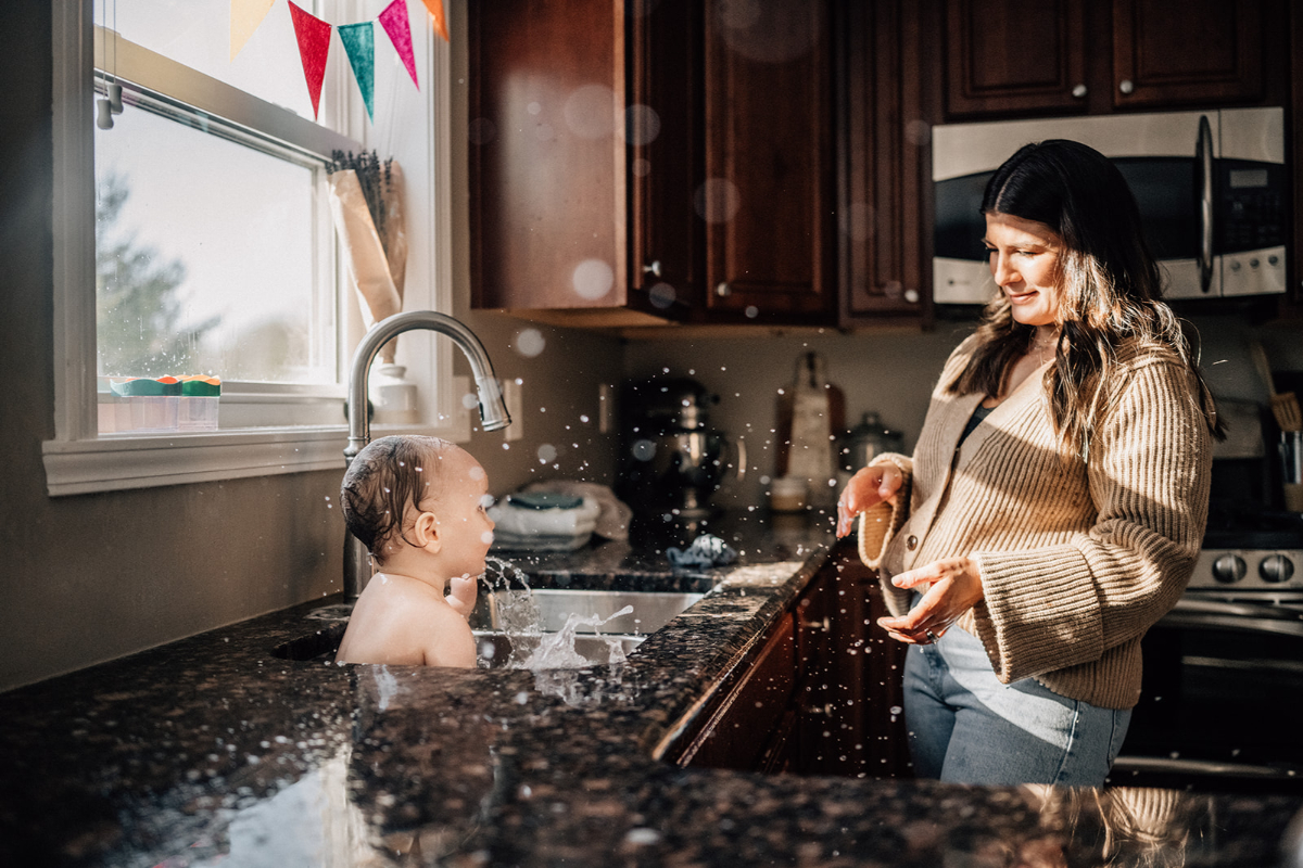 Parent washing baby in kitchen sink during baby’s first birthday session filled with playful moments