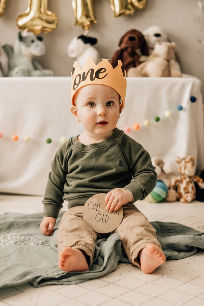 Baby wearing one crown during baby’s first birthday indoor session with simple decorations and soft light