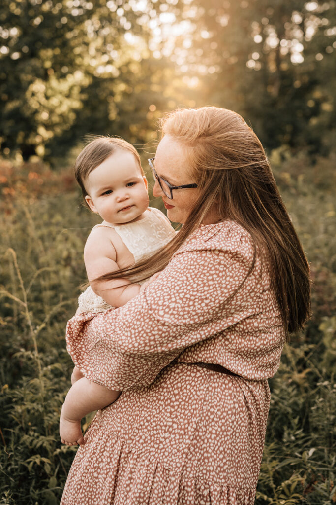 Mother holding baby close during baby’s first birthday session in warm outdoor golden light