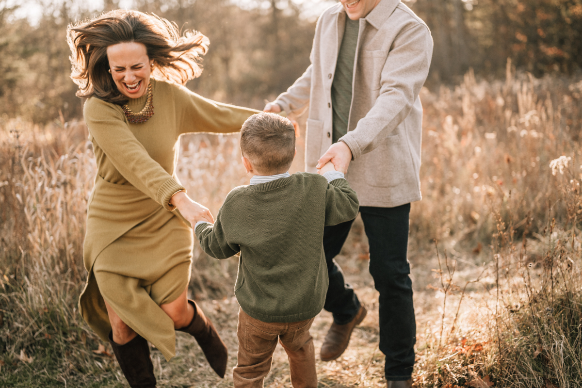 Family pictures in Saratoga Springs of parents spinning their son together in a golden autumn field.