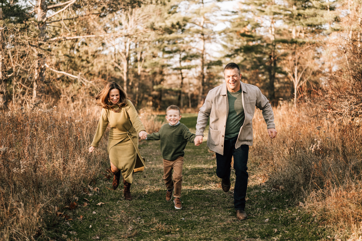Family pictures in Saratoga Springs of a family running and laughing together along a wooded trail.