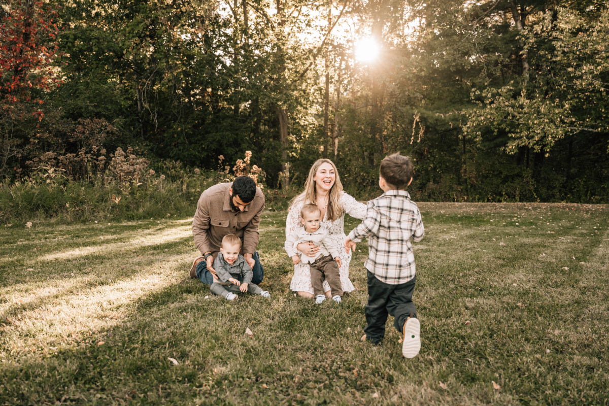 Family laughing and playing together in an open grassy field during golden hour.