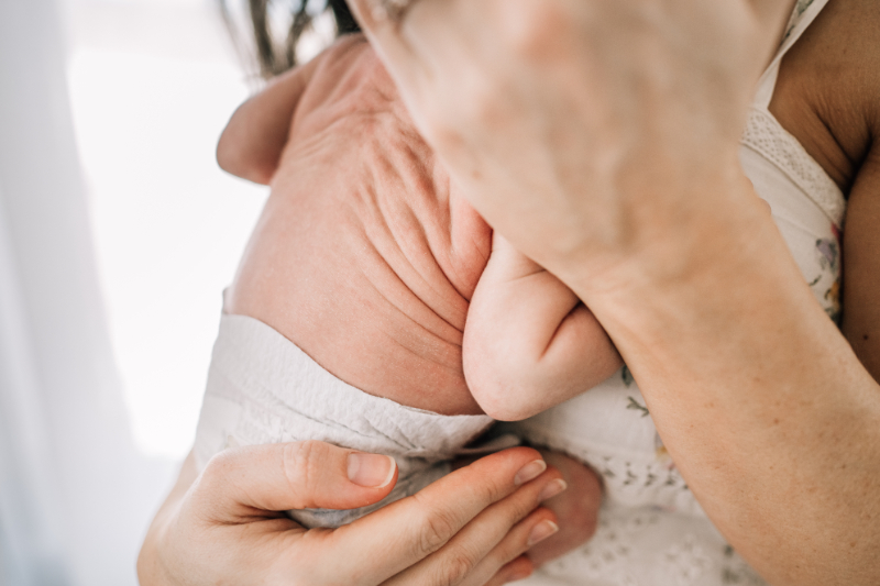 Close-up of newborn’s back in parent’s hands, showing soft textures and delicate detail.