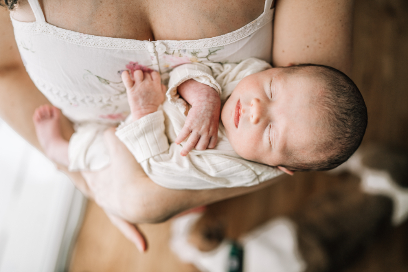 Mother holding sleeping newborn during newborn photos at home, capturing soft, overhead view and calm detail.