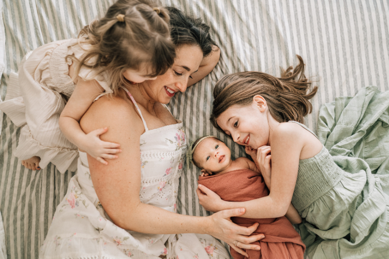 Mother and siblings snuggling newborn during newborn photos at home, capturing soft connection and loving interaction.