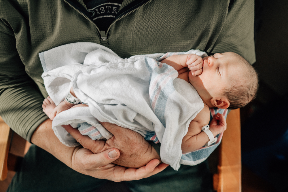Capturing sleeping newborn cradled in parent's arms during Fresh 48 session.
