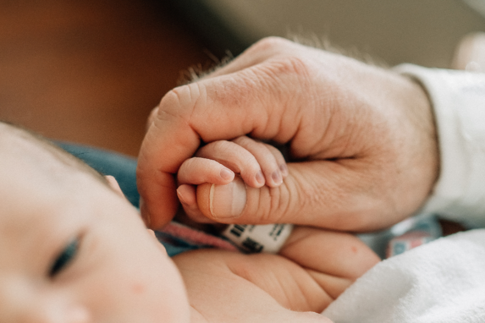 Newborn photographer near me capturing baby's tiny hand wrapped around a parent's finger.