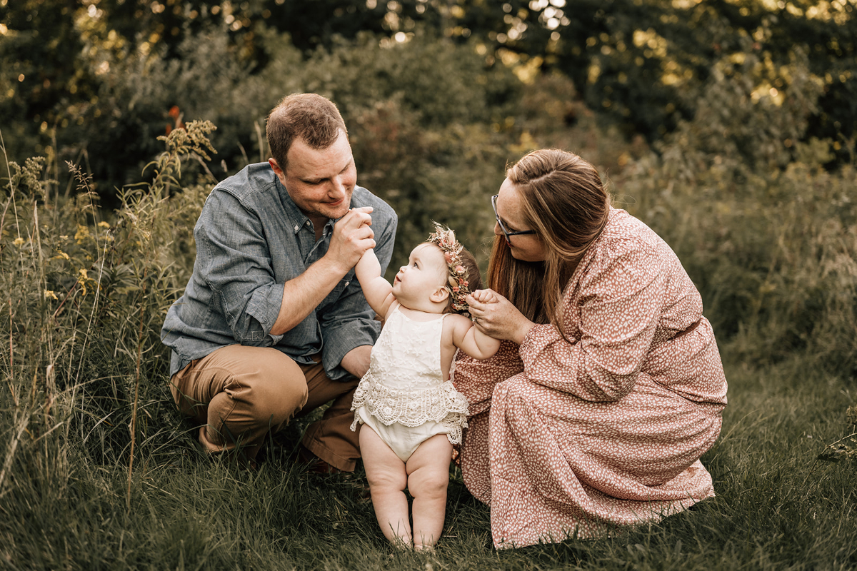 First birthday family photos of parents playing with their smiling one-year-old during an outdoor family session.