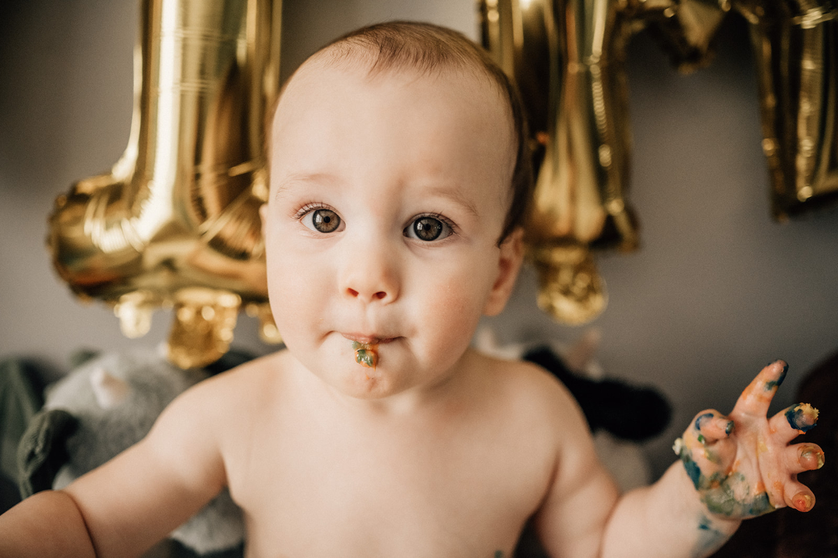 Close-up portrait of a one-year-old with birthday cake on their face during an in-home celebration.