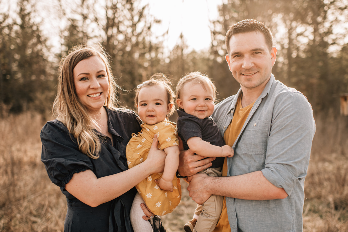 Parents holding their smiling twins during a relaxed outdoor family photography session at golden hour.