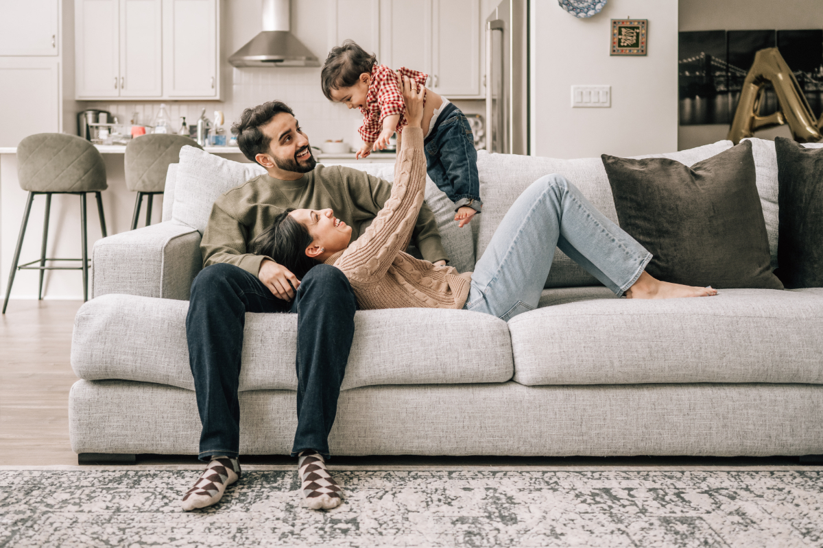 First birthday family photos of parents laughing while lifting their toddler during a cozy in-home session.