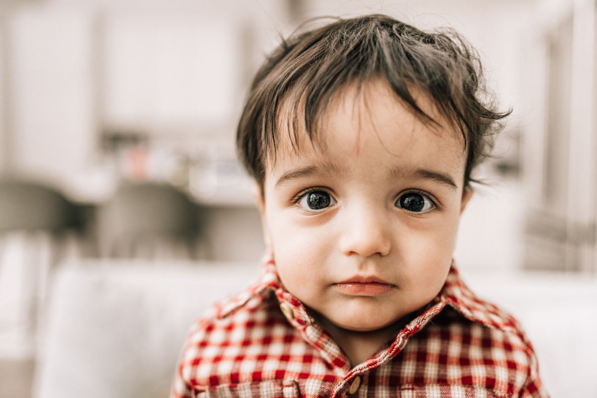 First birthday family photos featuring a close-up portrait of a curious one-year-old during an in-home celebration.