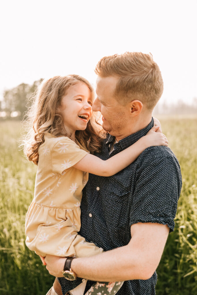 Candid family photos of a father holding his laughing daughter in a sunlit grassy field.