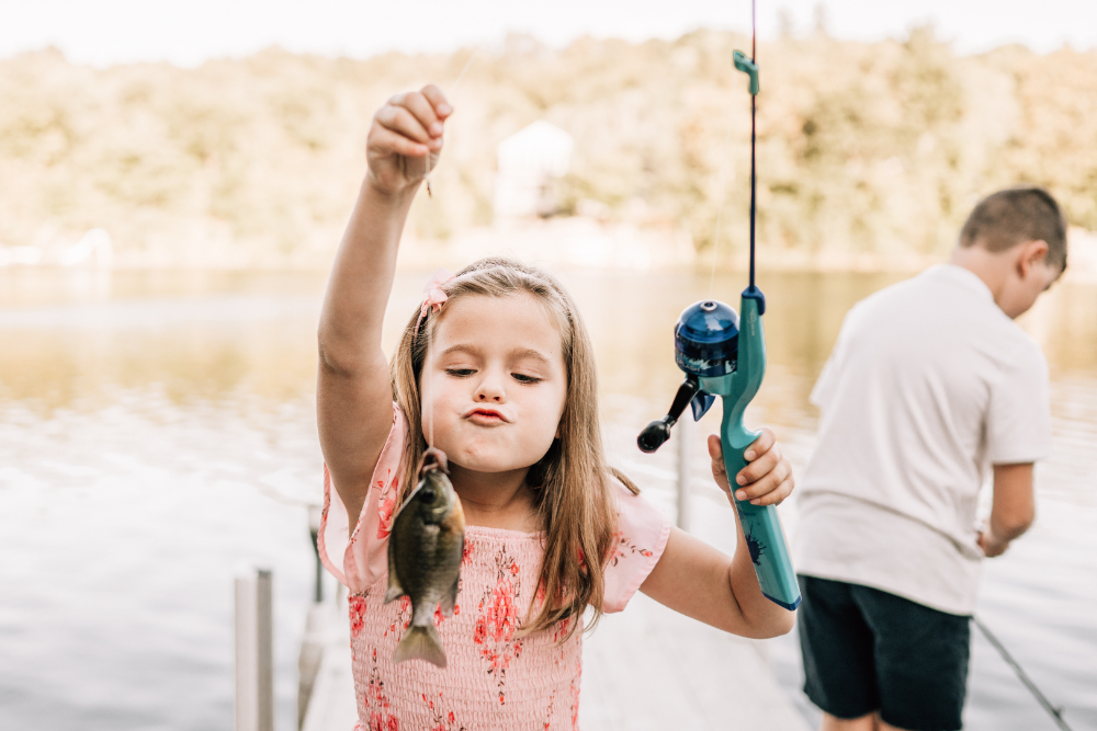 A young girl proudly holds up the fish she caught while fishing from the dock.