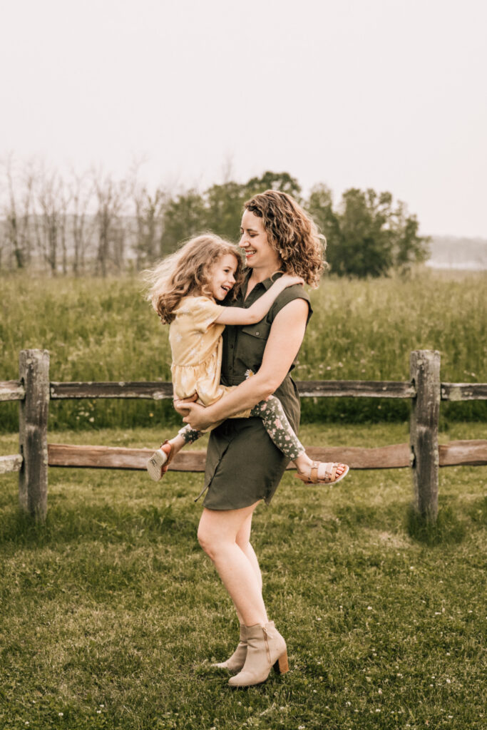 Candid family photos of a mother holding her laughing daughter while playing together in a field.