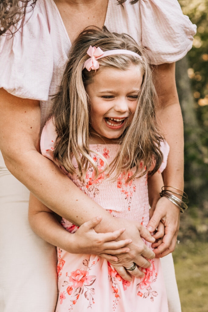 Candid family photos of a young girl laughing as her mother hugs her from behind.