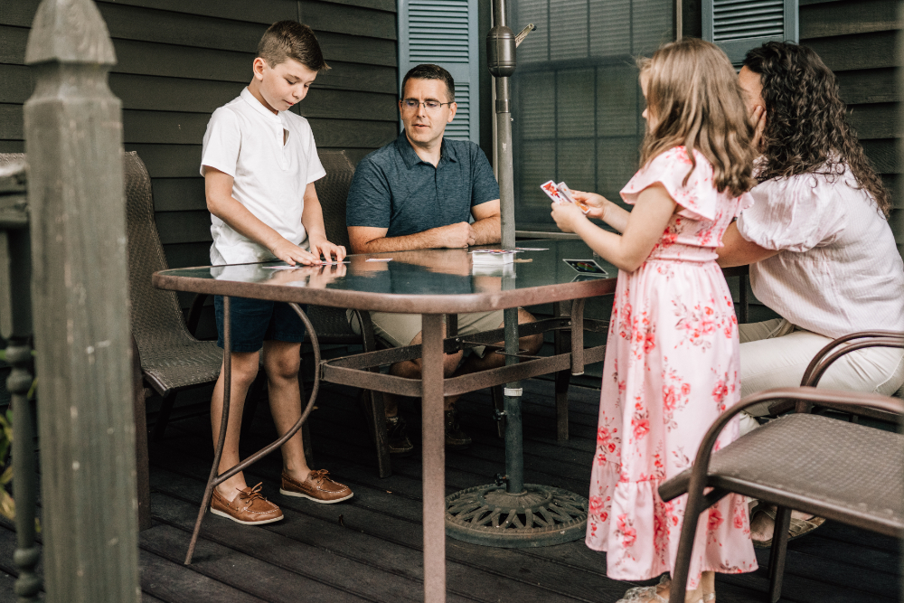 Candid family photos of a father and two children playing ping pong together outdoors at home.