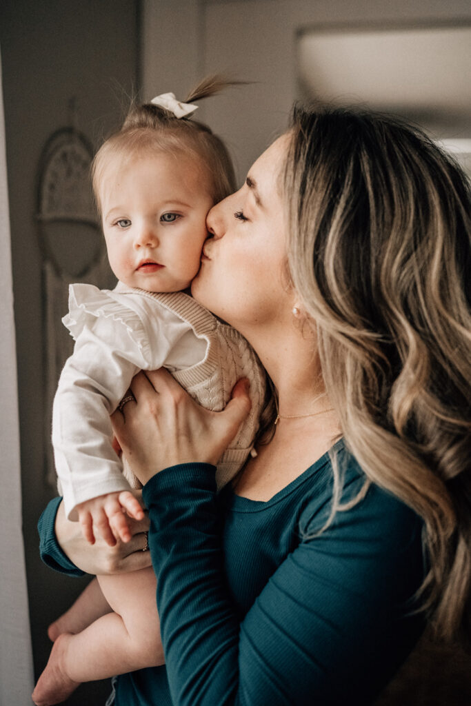 Family picture ideas at home with a mother holding her baby close and kissing her cheek.