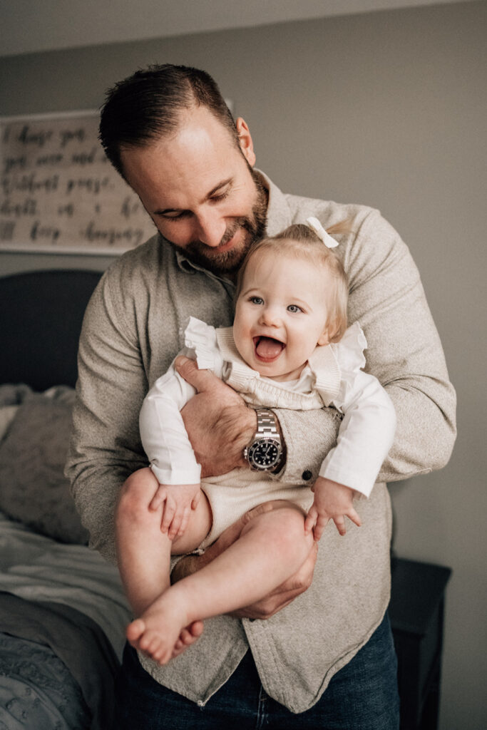 Family picture ideas at home with a smiling father holding his laughing baby in his arms.