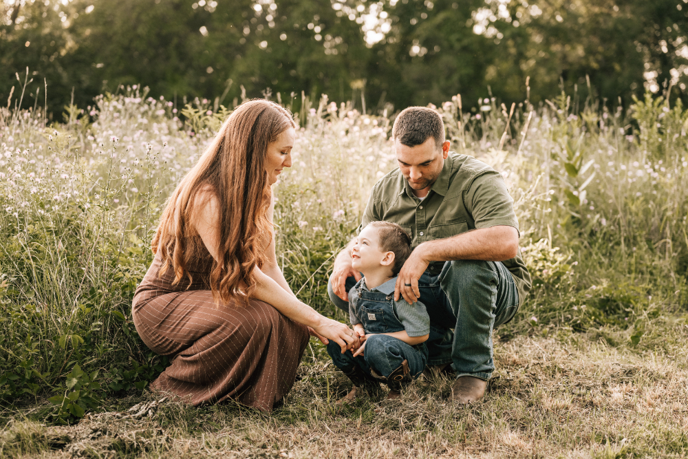 Lifestyle family photography of parents sharing a quiet moment with their young child in a wildflower field.