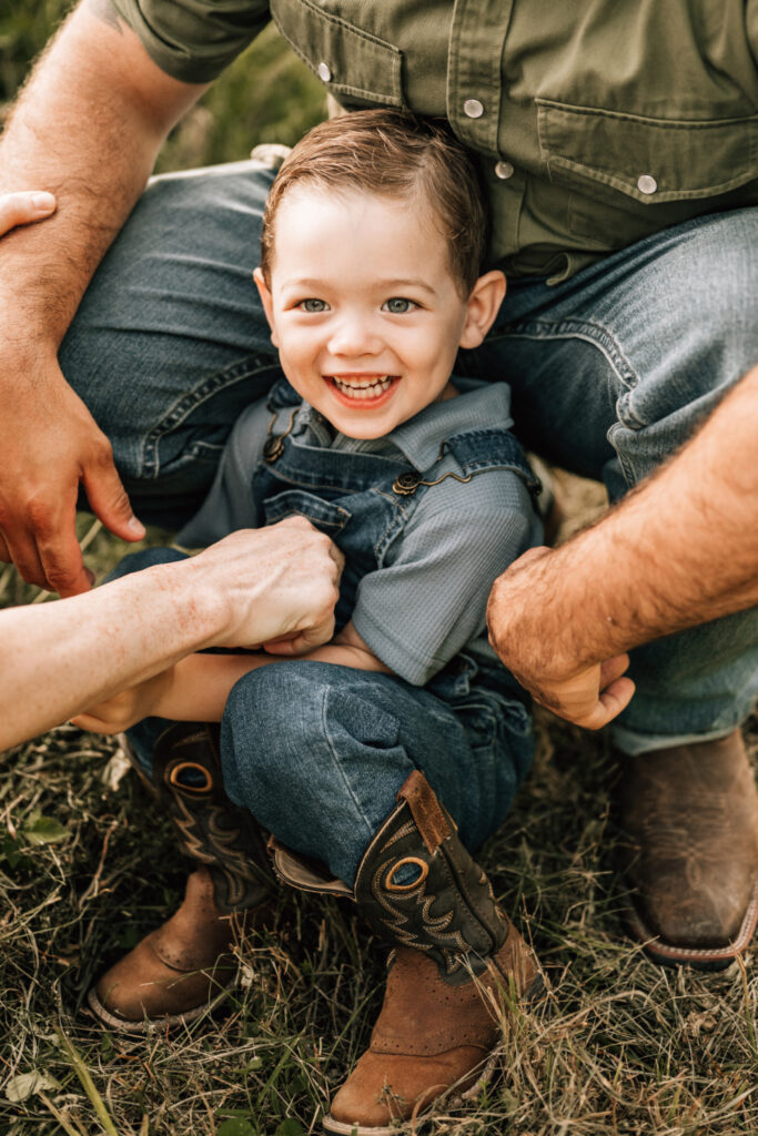 Lifestyle family photography captures a young child’s genuine smile while sitting close with family outdoors.