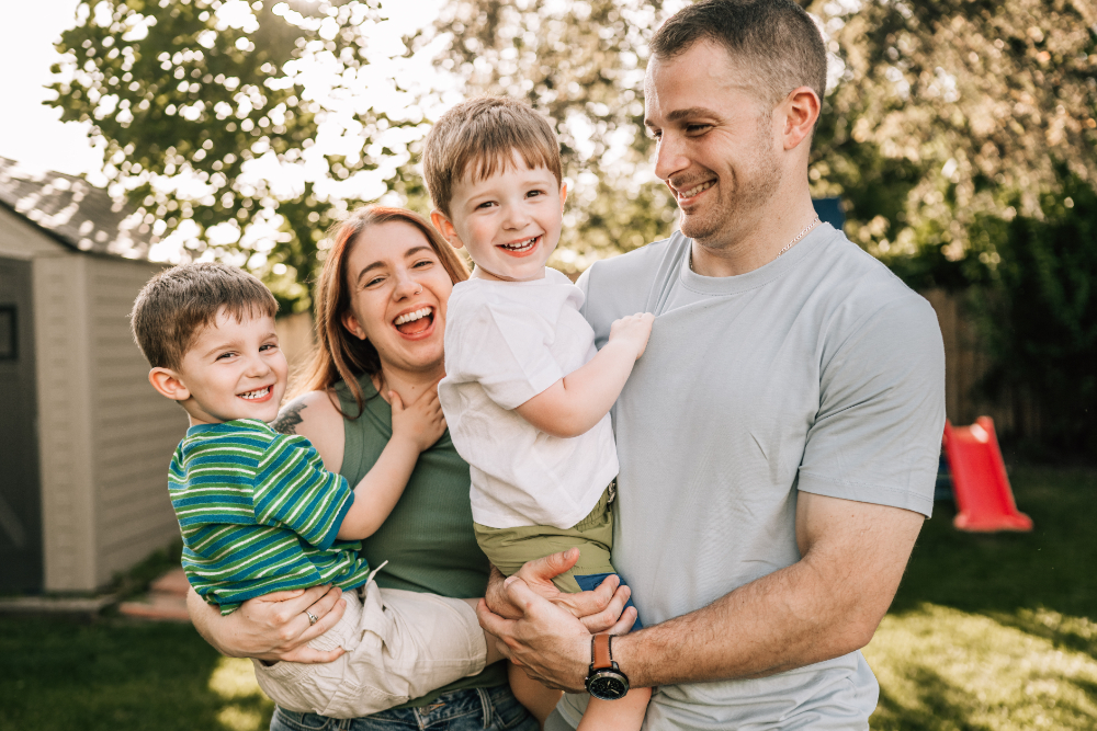 Parents holding their two smiling sons during a joyful backyard family photography session at golden hour.