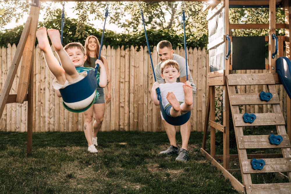 Outdoor family photo ideas with parents pushing children on swings during a playful backyard family session.