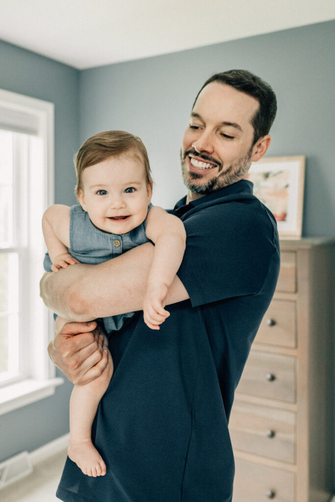 A parent holds their smiling baby during a relaxed moment together at home.