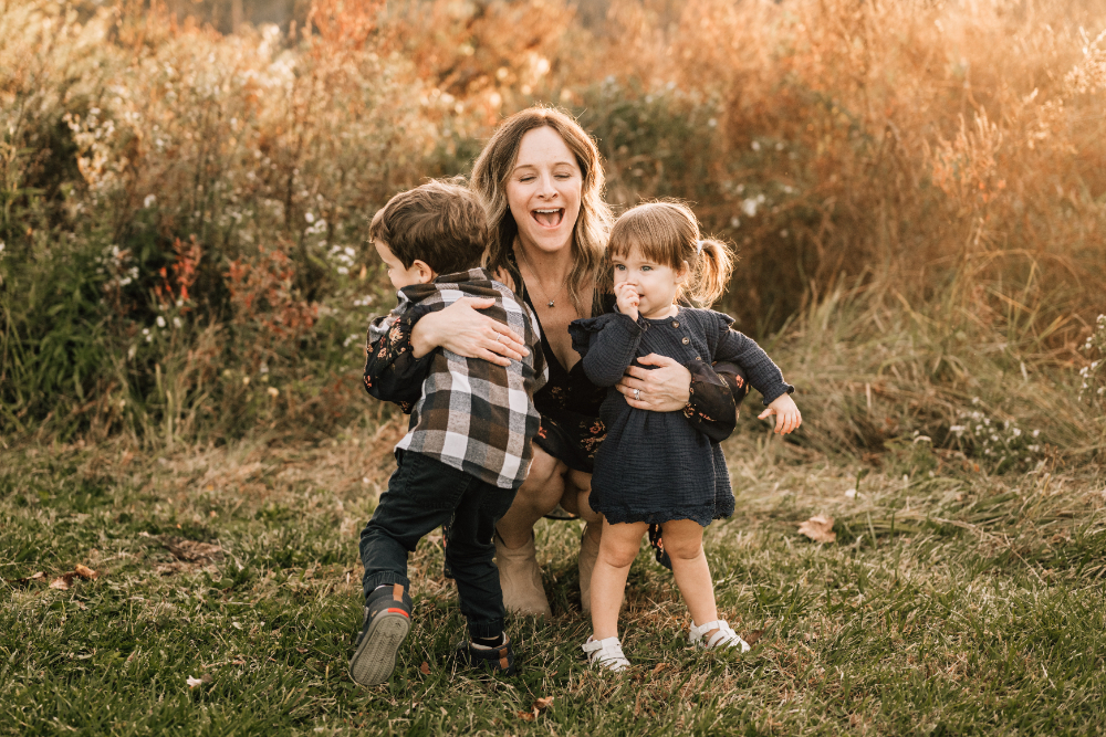 Mother laughs while hugging her two young children during a joyful outdoor fall family session.