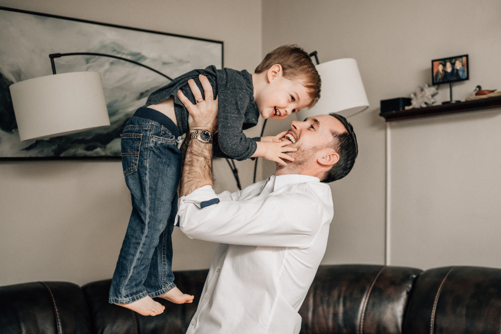 At home family photos of a father lifting his smiling toddler during a playful moment together.