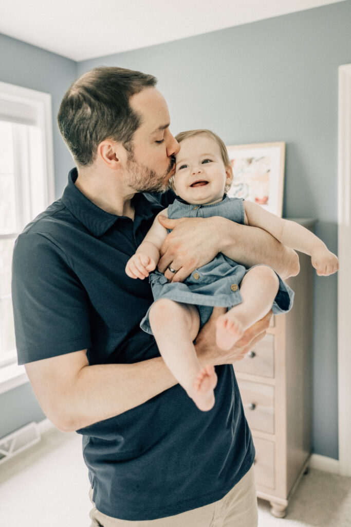 At home family photos of a father holding and kissing his smiling baby at home.